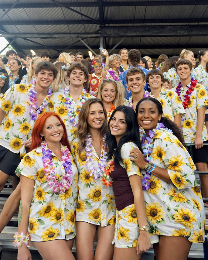 Large group of young people at stadium stands wearing matching sunflower print Hawaiian shirts and leis