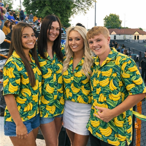 Four friends smiling at a stadium, wearing matching green Hawaiian shirts with banana print