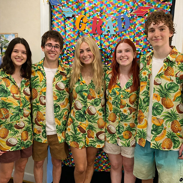 Five friends wearing matching pineapple and coconut print Hawaiian shirts, posing in front of a colorful graduation backdrop